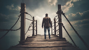 A person in a brown jacket stands on a wooden bridge under a dramatic cloudy sky, overlooking the ocean. The mood is contemplative.