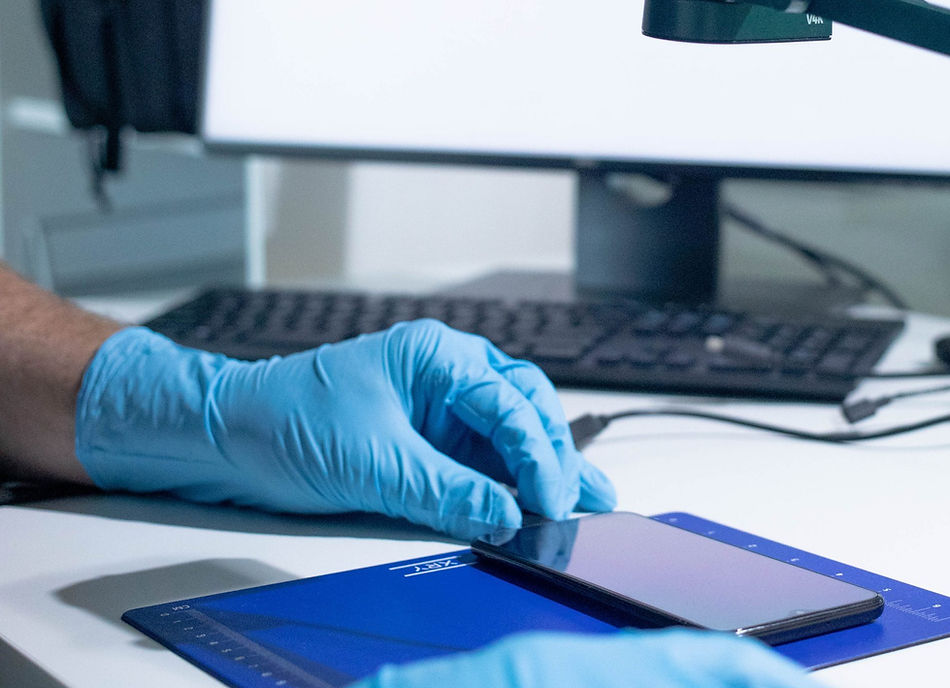 Data recovery technician in gloves handling smartphone on anti-static mat during mobile phone repair and recovery.