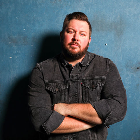 Country singer-songwriter Matt Rogers wearing a black denim jacket against a blue wall