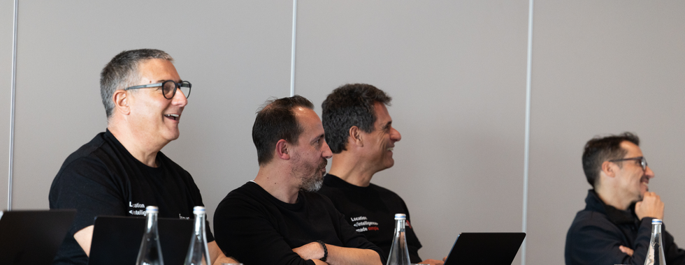 Founders sit at a meeting table with laptops and water bottles, focused on the ongoing quarterly meeting.