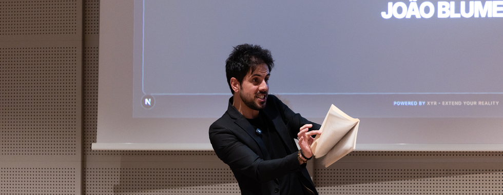The presenter gestures animatedly while holding folded papers during the interactive team activity.