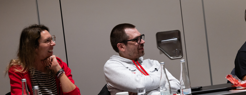 Two colleagues laugh while seated at a conference table with notebooks, water bottles, and small wrapped candies.