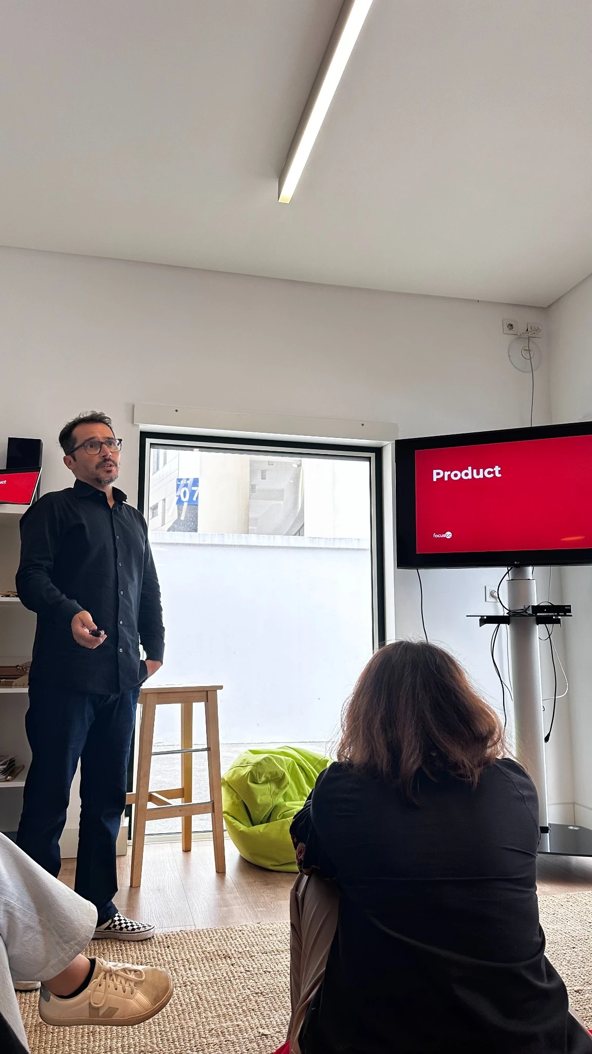 Team member presenting a “Product” slide on a screen to colleagues seated in an informal meeting space.