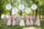 Wedding party in suits and pink dresses, smiling under green trees. Speech bubbles indicate some rented, some bought suits.