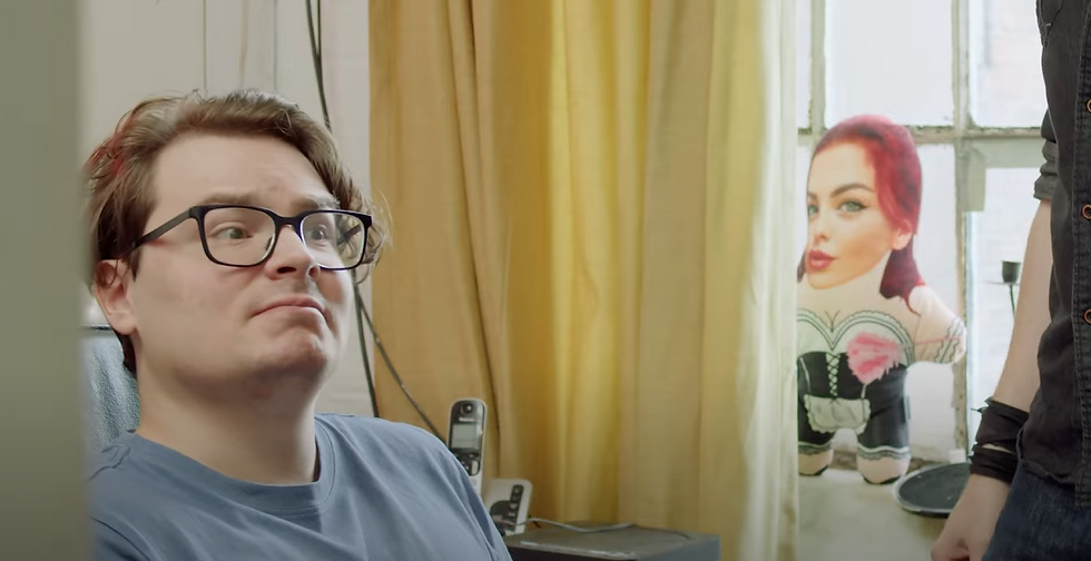 A man with glasses looking scared while a toy of Rebecca Goodwin looks at him.