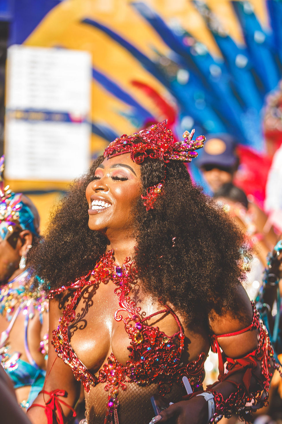 Carnival masquerader in a vibrant red beaded costume and feathered headpiece celebrating on the parade route as part of The Gift of Carnival graduation experience