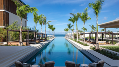 The long palm-lined infinity pool at Silversands Grenada on Grand Anse Beach, stretching toward the Caribbean Sea past lounge chairs and cabanas.
