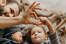 A father and two children forming a heart shape with their hands, lying together on a bed.