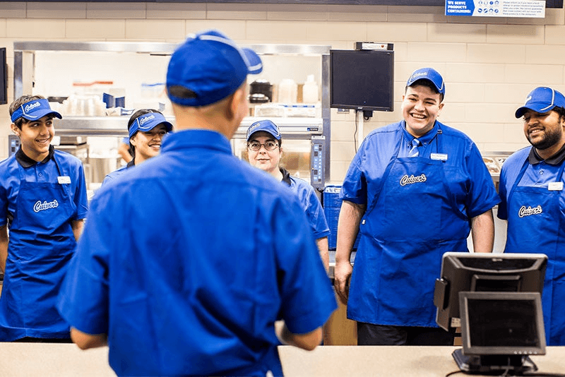 Group of employees wearing blue uniforms, interacting joyfully in a restaurant setting.