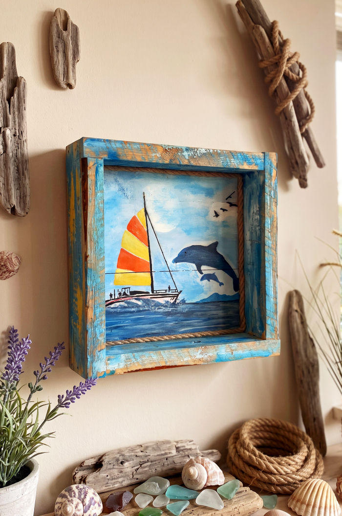 Tableau artisanal unique en bois de pin massif représentant un voilier et deux dauphins sur l'océan.