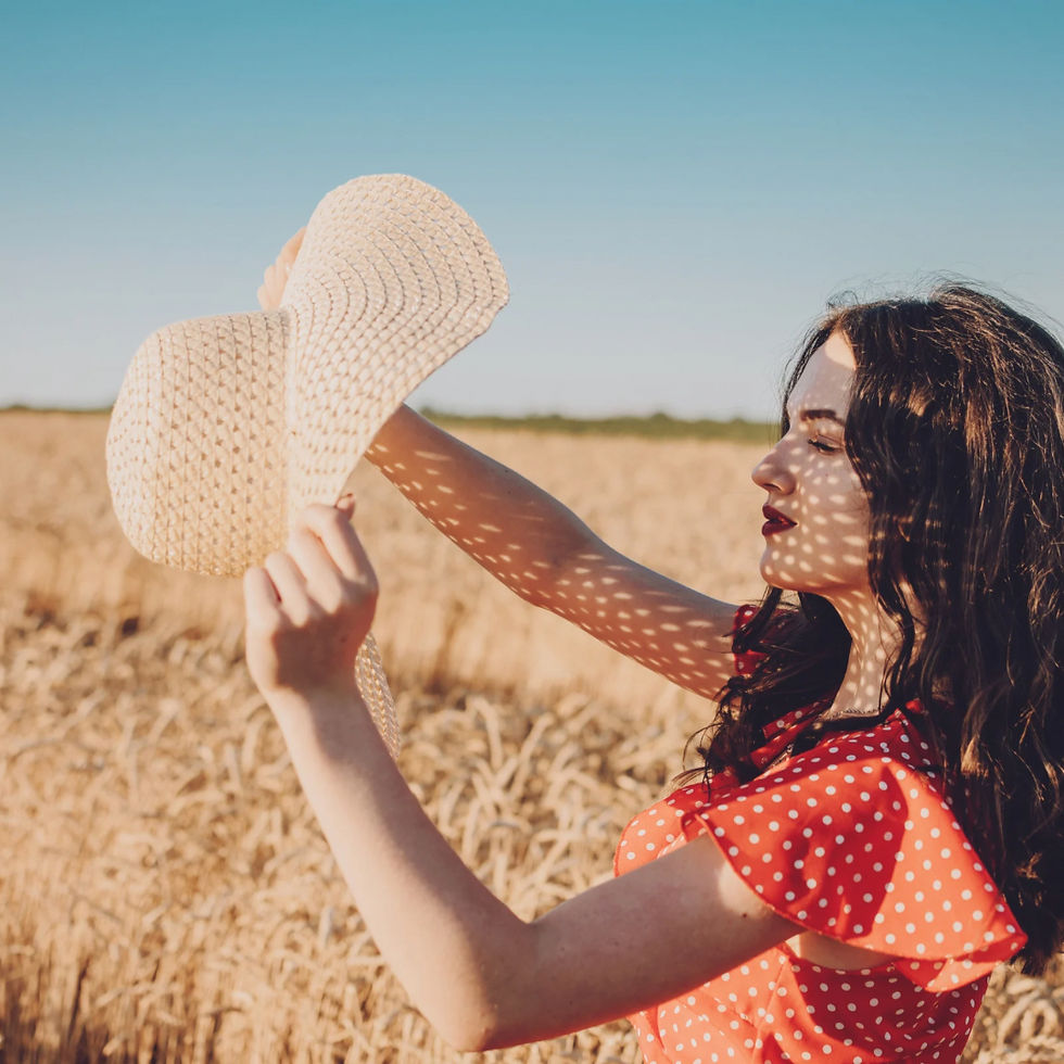A woman in a red dress with long hair in a wheat field holding a hat in the sun.