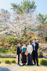 満開の桜の下、旧吉田茂邸で美しく着飾った姉妹が笑顔で並ぶ卒業記念の家族写真。春のやわらかな光に包まれた、家族の温かな思い出を写した一枚。