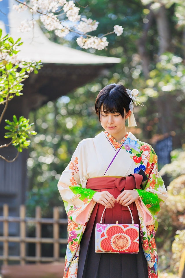 満開の桜の下、旧吉田茂邸で美しく着飾った姉妹が笑顔で並ぶ卒業記念の家族写真。春のやわらかな光に包まれた、家族の温かな思い出を写した一枚。