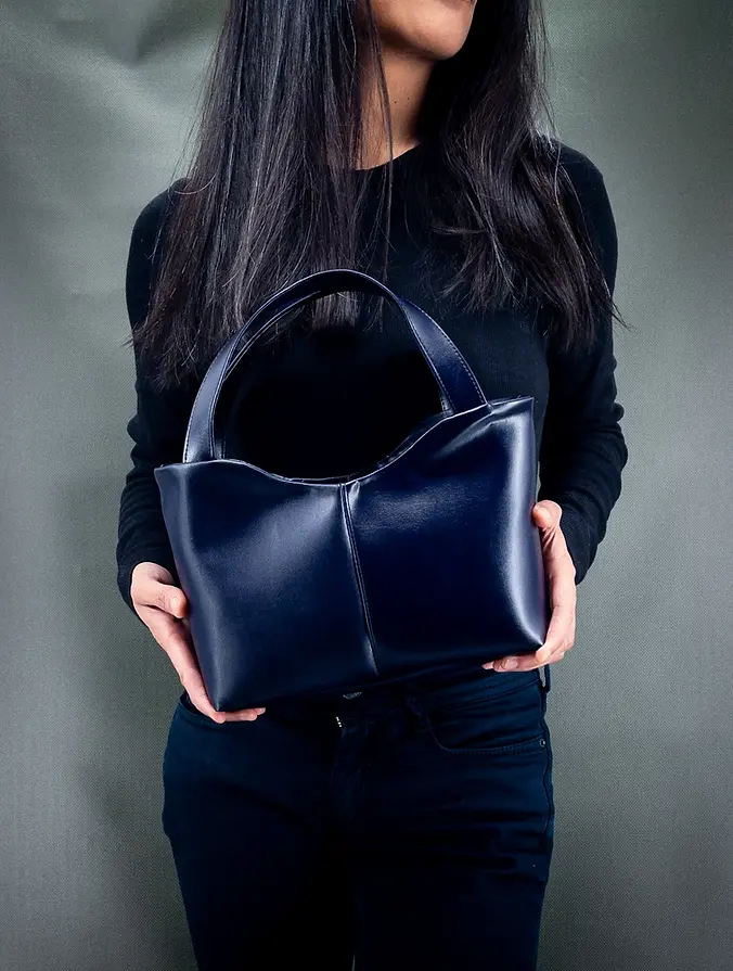 Lubay vegan handbag, Scaldis M model in violet almost blue leap, held by a woman dressed in black against a dark green background.