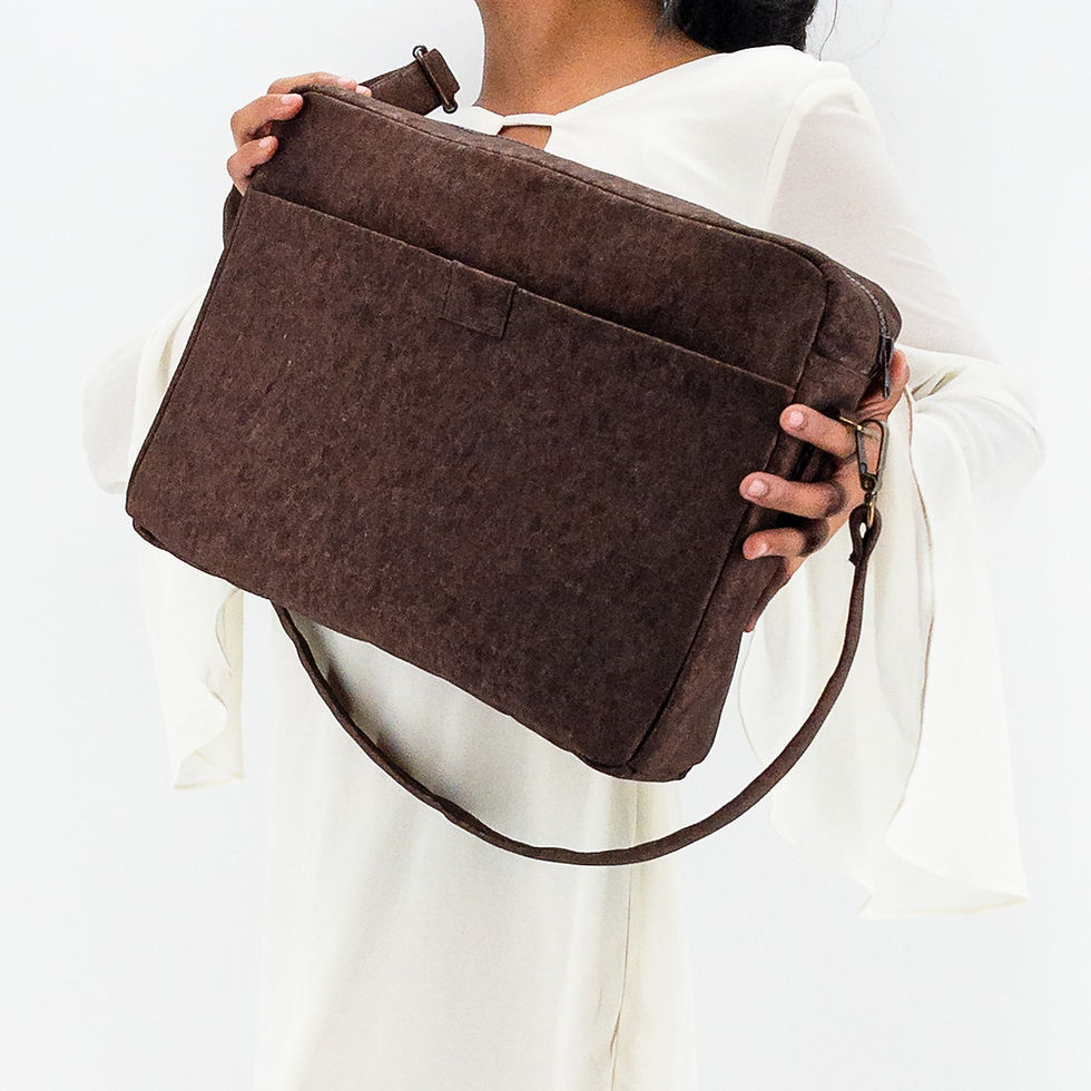 Thumbnail: Femme habillée en blanc tenant en main le sac pour ordinateur vegan Woluwe en liège chocolat de Lubay, sur fond clair