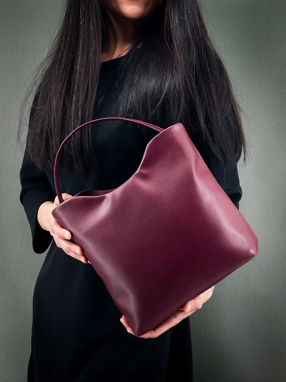 Miniature : Sac à main vegan Lubay, modèle Mosa, Grape Skin vin, porté à la main par une femme habillée en noir sur fond vert foncé.