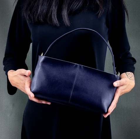 Sac vegan Lubay Ieper 25 en leap violet almost blue, tenu en main par une femme habillée en noir sur fond vert foncé.