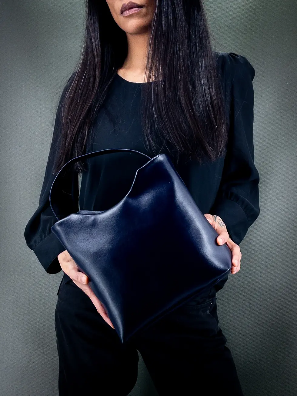 Miniature : Sac à main vegan Lubay, modèle Mosa, LEAP violet almost blue, porté à la main par une femme habillée en noir sur fond vert.