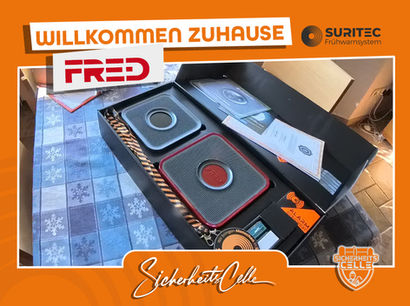Geöffnetes FR.ED Frühwarnsystem-Set von Suritec liegt auf einem Tisch. Zu sehen sind Geräte, Zubehör und Anleitungen. Text: Willkommen Zuhause FR.ED.
