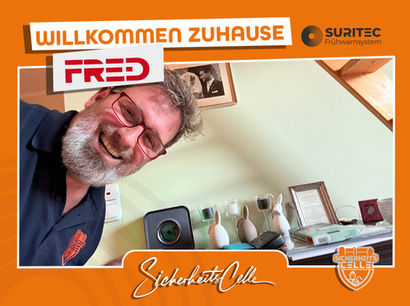 Björn Emanuelsson von SicherheitsCelle lächelt neben einem installierten FR.ED Frühwarnsystem. Text: Willkommen Zuhause FR.ED, Logos von Suritec und SicherheitsCelle.