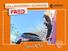 Björn Emanuelsson von SicherheitsCelle montiert ein FR.ED Frühwarnsystem an einer Hauswand. Unten steht das Firmenfahrzeug. Text: Willkommen Zuhause FR.ED.