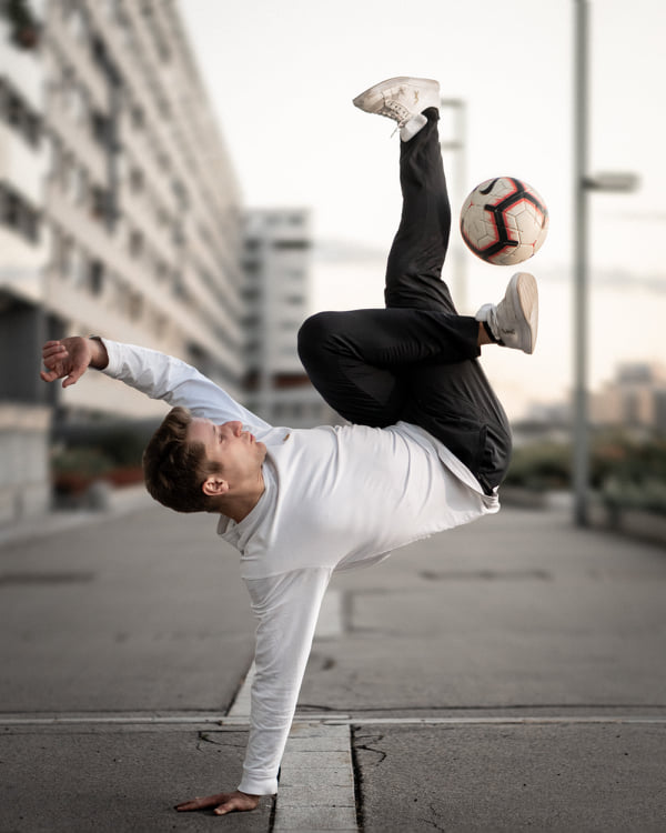 Martin Schopf in a one-hand stand on a street, the ball floating above his feet