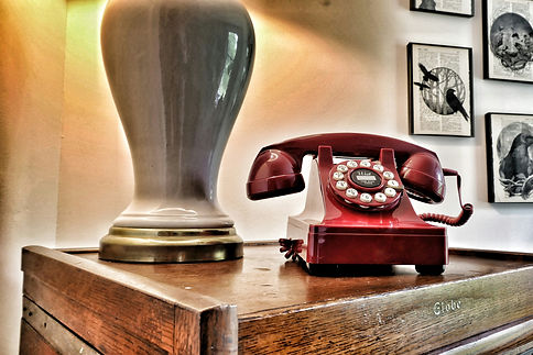 A photo of a red rotary phone on a side table next to a lamp signifying that you can contact Paul Freiberger and Shimmering Careers multiple ways during your job search.