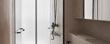 Spacious neutral-toned bathroom featuring a wall-hung toilet, glass shower partition, floating vanity, and warm sconce lighting.