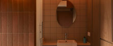 Warmly lit vanity area with an oval mirror, concealed cove lighting, terracotta tones, and custom wood veneer panelling.