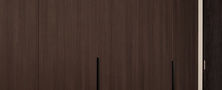 Sleek master bedroom wardrobe design featuring full-height dark wood joinery and a modern minimalist dressing stool.