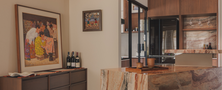 Modern kitchen area featuring a raw reddish stone island, low credenza with artwork, and tall timber cabinets with glass pocket doors.
