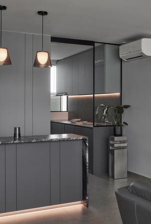 A grey kitchen island with hanging pendant lights next to a black-framed glass wall.