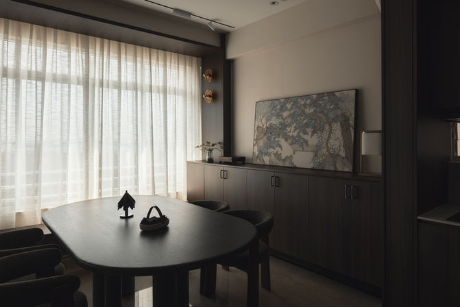 A wide view of a minimalist dining room with a long dark table and built-in cabinetry.