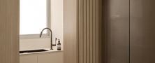 Framed doorway transition featuring light timber fluted wall panelling and view into modern white kitchen.