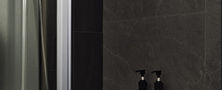 Contemporary shower stall design featuring dark marble-look wall tiles, stainless steel fixtures, and built-in vanity ledge.