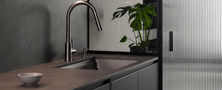Minimalist dark kitchen workspace featuring dark counter, undermount sink, LED under-cabinet lighting, and fluted glass door partition.