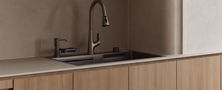 Clean kitchen workspace detail showcasing light timber cabinets, brass goose-neck faucet, undermount sink, and light stone countertop.