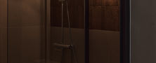 Contemporary bathroom shower design featuring dark wall tiles, glass partition, overhead rain shower, and warm globe wall sconces.