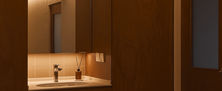 Modern vanity area with a backlit floating mirror, full-height timber cabinet panel, and ambient warm lighting.
