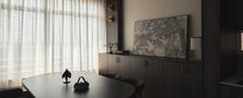 Serene minimalist dining space featuring a dark curved oval table set, low credenza storage, framed artwork, and sheer curtains.