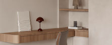 Compact home office nook built into living space featuring floating timber desk, recessed wall shelves, minimalist chair, and ambient lamp.