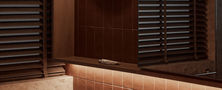Moody Japandi washroom vanity featuring textured stone wall paneling dark timber mirror frame and warm wall sconce.