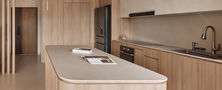 Spacious open-plan kitchen featuring a large curved island counter, warm oak cabinets, white overhead storage, and seamless transitions.