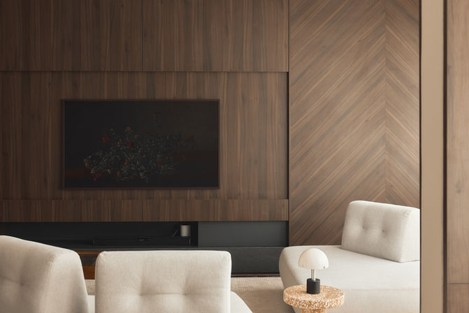 A living room featuring a large wood-paneled wall with a television and light-colored lounge chairs.