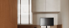 Minimalist Japandi bedroom study corner featuring a floating timber desk black wooden chair white cabinet and window Venetian blinds.