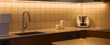 Modern kitchen interior featuring warm timber joinery, under-cabinet strip lighting, and earth-toned ceiling accents.