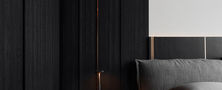 Atmospheric dark bedroom bedside corner featuring fluted accent wall, dark upholstered headboard, and minimalist nightstand.