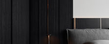 Atmospheric dark bedroom bedside corner featuring fluted accent wall, dark upholstered headboard, and minimalist nightstand.