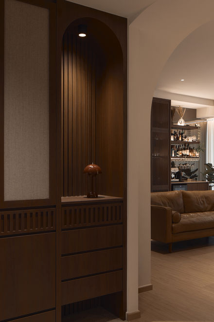 A view from a hallway showing custom dark timber cabinetry with fluted details beneath a plaster archway, looking through into a warm, sunlit open-plan living area.