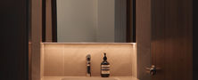 Warm minimalist bathroom vanity area with LED backlighting behind a rectangular mirror and sleek dark counter basin.